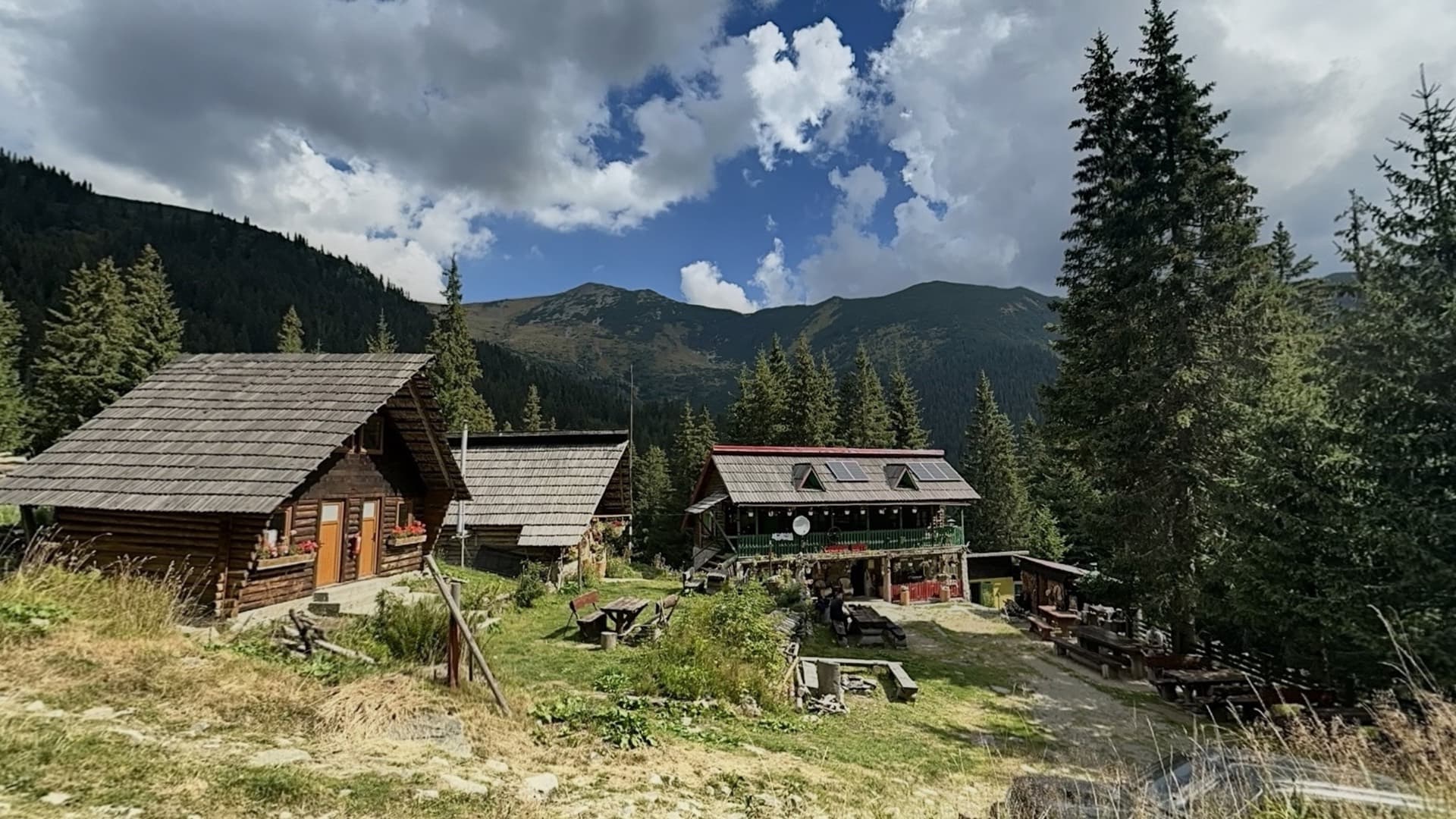 Cabanele de lemn în poiană, cu creasta Retezatului în spate